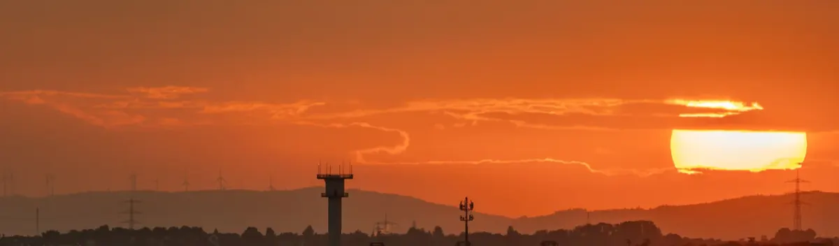Airport control tower and radio mast against a sunset sky